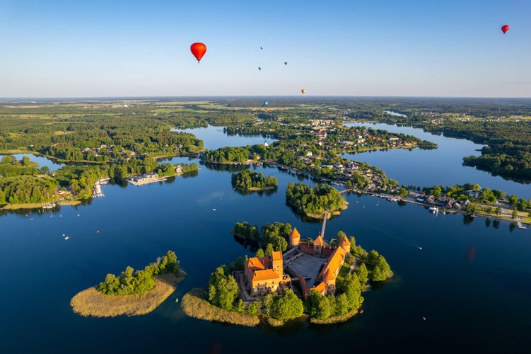 Photoof Aerial summer sunny sunset view of Trakai Island Castle and hot air balloons, Lithuania.