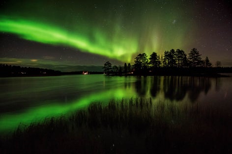 Photo of northern lights and it's reflection in the lake in Kuusamo, Finland.