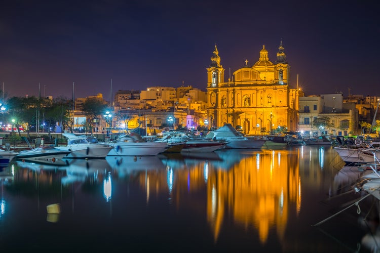 Photo of Msida, Malta - The beautiful Msida Parish Church with yachts and boats and reflection on the water by night.