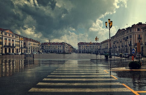 photo of Pedestrian crossing and big plaza at city center under cloudy sky at rainy day in Cuneo, Italy.