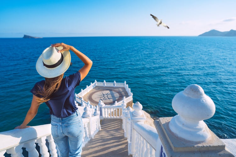 Photo of young tourist woman in sun hat enjoying sea view at Balcon del Mediterraneo in Benidorm, Spain.