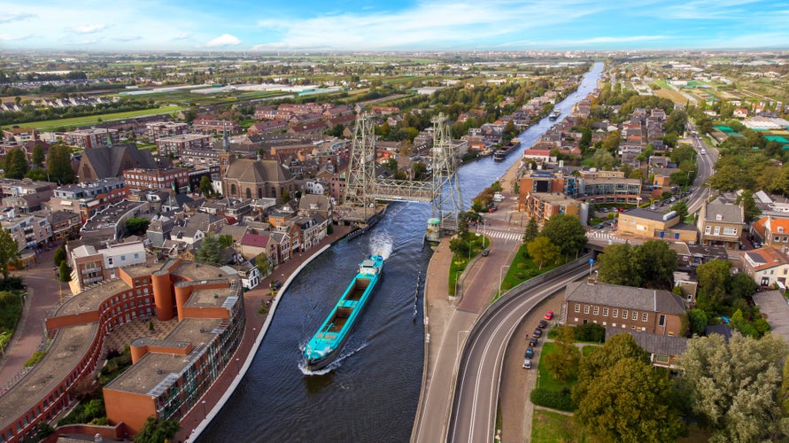 photo of view of Aerial drone view of the Gouwe canal with a historical lift bridge (Dutch: Hefbrug) in Boskoop opened for some cargo ships coming from the inland terminal of Alphen aan den Rijn called 'Alpherium'., Alphen aan den Rijn, the Netherlands.