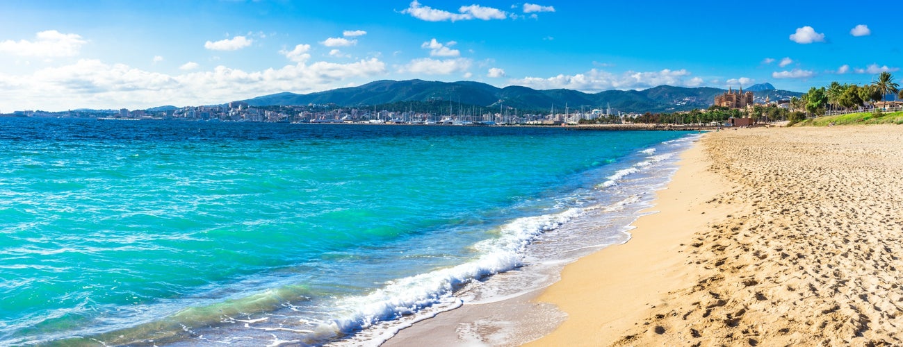 Photo of the beautiful beach in Palma de Mallorca with the town and harbor in background, beautiful coastline