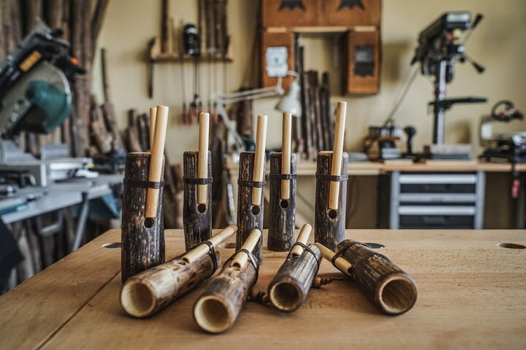 A collection of handcrafted wooden whistles with bamboo mouthpieces is displayed on a workbench in a rustic workshop setting in Almeria..png