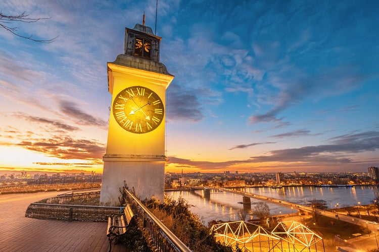 Photo of sun sets over Novi Sad, the iconic clock tower of Petrovaradin Fortress stands tall, offering a picturesque view of Serbian history and culture.