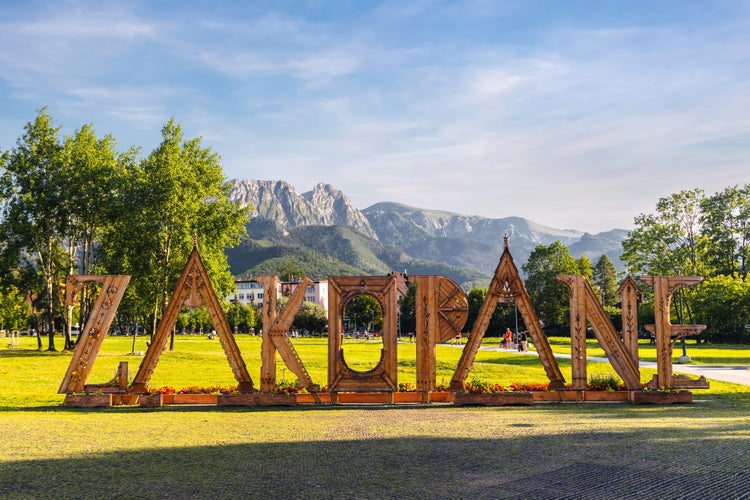 Wooden letters - landmark sign with the name of the city. Panoramic scenic landscape view of High Tatra Mountains peaks and Giewont in background. Rowien Krupowa park, Zakopane, Poland.