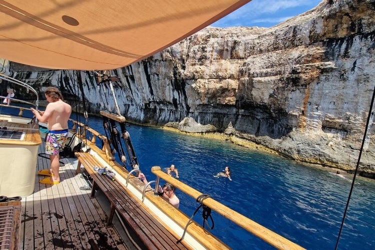 People swim in the clear blue waters near rocky cliffs at Kornati National Park, viewed from a wooden boat deck with shade overhead..jpg