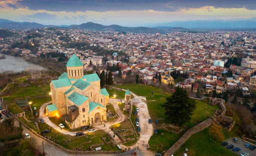 Photo of drone of illuminated rebuilt building of Cathedral of Dormition, temple of Georgian Orthodox Church in Kutaisi against cityscape on spring evening.