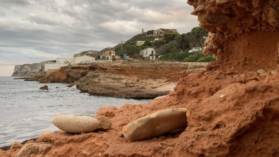 photo of view of Captured in Las Rotas, Spain, a wave breaking against rocks. Blue sky on an evening with a subtle red tint in the clouds during light cloud cover. Romantic scenes at the sea with rocks.