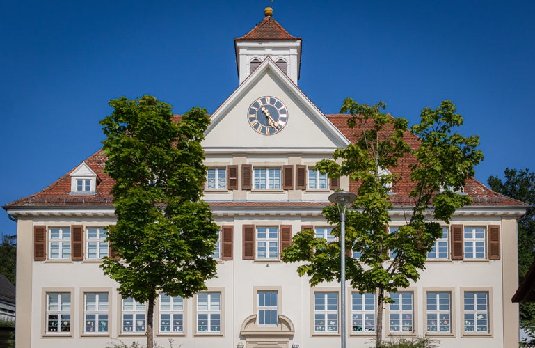 photo of view of Old school house also used as the local city hall with trees in foreground in Waldhilsbach, a small village near Heidelberg in Baden-Württemberg Germany.