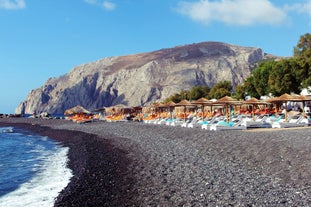 Photo of aerial view of black Perissa beach with beautiful turquoise water, sea waves and straw umbrellas, Greece.