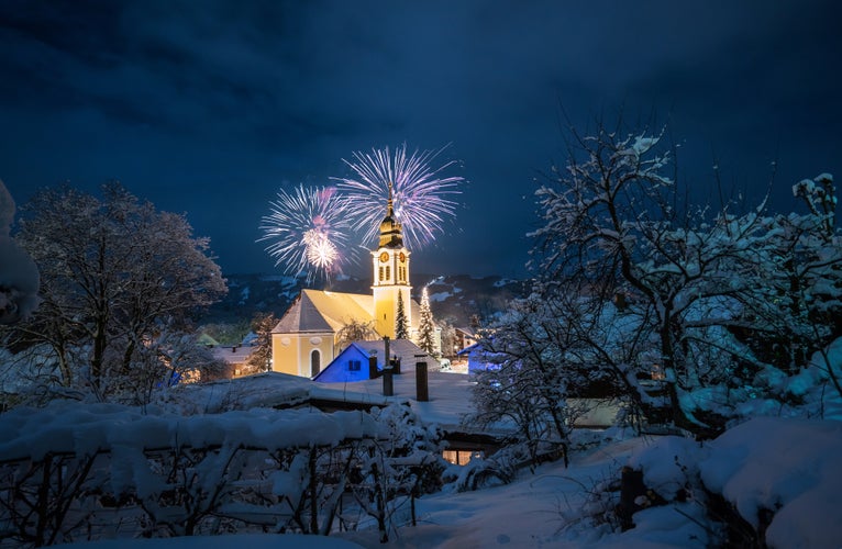 Long exposure of a church in a snowy winter landscape by night with fireworks, celebrating the new year in the city Sonthofen in Germany