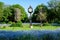 Photo of beautiful landscape with green trees, leaves, vintage clock and many small blue forget me not or Scorpion grasses flowers in a sunny day at the entry to Cismigiu Garden (Gradina Cismigiu) in Bucharest, Romania.