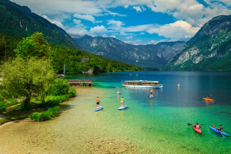 Healthy sporty friends exercising on the colorful sup boards. Active men friends kayaking on the lake Bohinj, Ribcev Laz, Slovenia, Europe