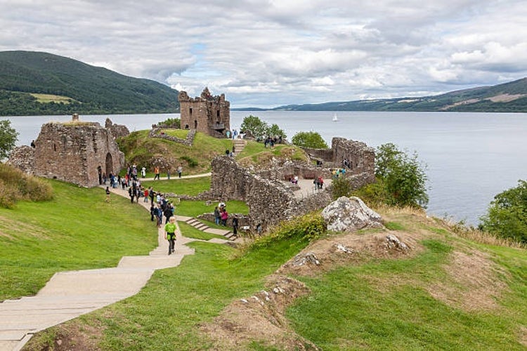 Urquhart Castle overlooking the waters of Loch Ness, filled with visitors walking through its ancient ruins.jpg