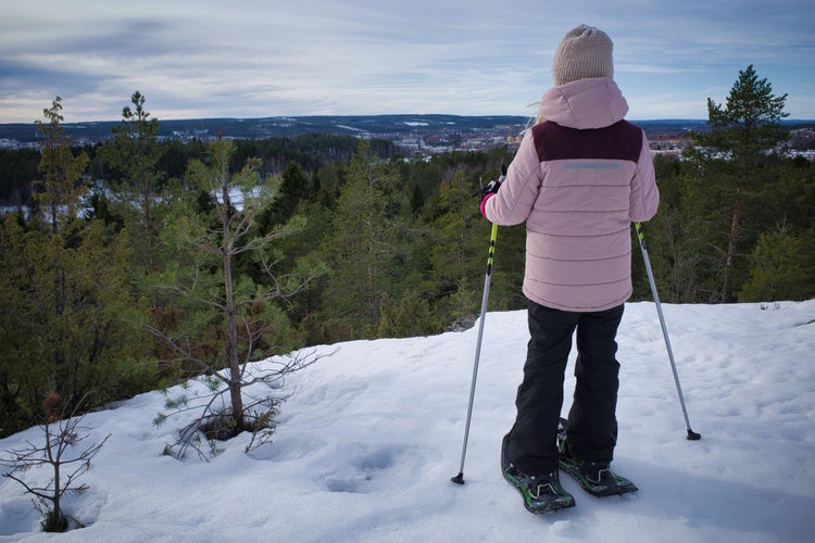 photo of view of Young girl walking with snow shoes looking over vast landscape in horizon. View over Skellefteå, Sweden.