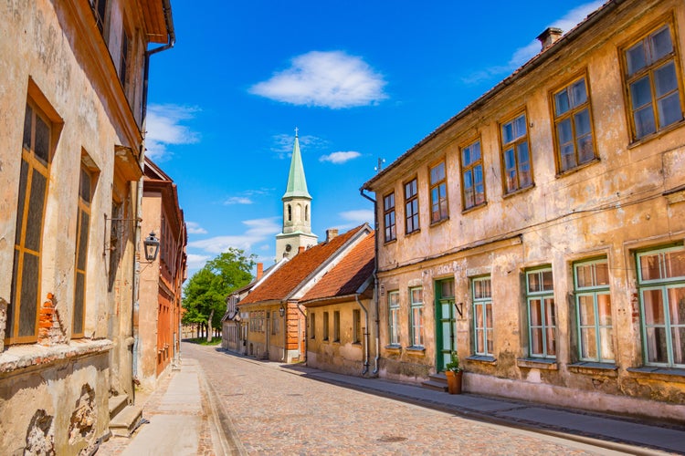 KULDIGA, LATVIA -  Old houses with collapsed plaster and the Evangelical Lutheran Church of Saint Catherine (Kuldīgas Svētās Katrīnas evaņģēliski luteriskā baznīca) along a cobbled road