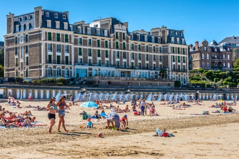  People sunbathe on fine sand by blue and white striped beach tents on Plage de l'Écluse, the main beach of this popular French seaside resort.