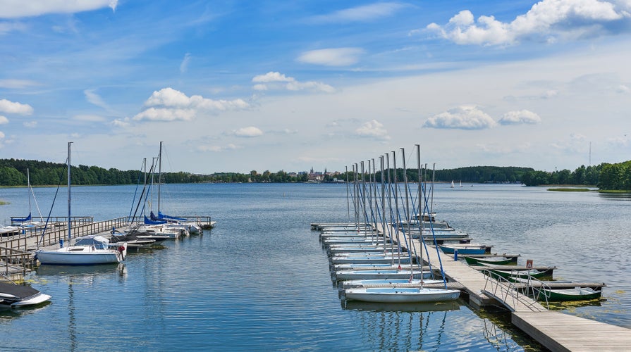 Beautiful landscape presenting sailboats and motorboats moored to the pier in the bay of the lake in the port against the background of clouds and blue sky on a sunny day in Olsztyn in Warmia and Mazu