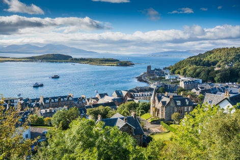 photo of view of Aerial view of small town Oban in Scotland. Scattered trees, small village and sea in the background, bright sunny day.