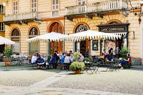 Turin, Italy. In Piazza della Consolata, under large umbrellas, outdoor tables of a cafeteria with some people sitting.