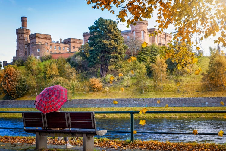 Photo of tourist woman holding a scottish flag umbrella enjoys the view of the skyline of Inverness during a sunny autumn day, Scotland.