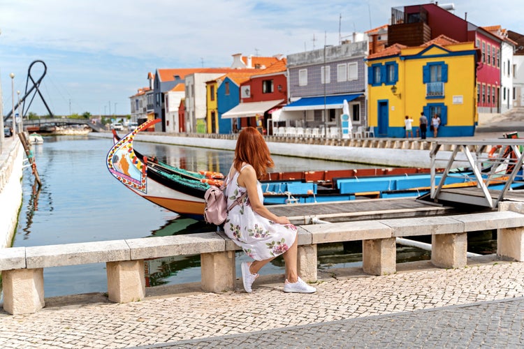 A woman traveler with red hair seat near traditional boats on main city canal in Aveiro, Portugal