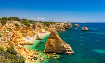 Photo of beautiful aerial view of the sandy beach surrounded by typical white houses in a sunny spring day, Carvoeiro, Lagoa, Algarve, Portugal.