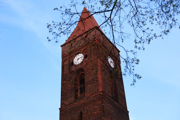 photo of view of Clock tower in the old town. Clock in Poland, Lubin. European architecture of the past. The clock tower on the background of the blue sky behind the tree branches