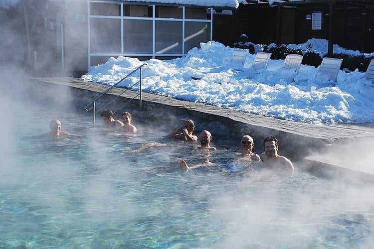 People relaxing in a steaming outdoor thermal pool surrounded by snow-covered ground..jpg