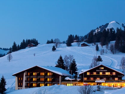 photo of Arvenbüel Hotel at winter covered with snow at night in Switzerland.