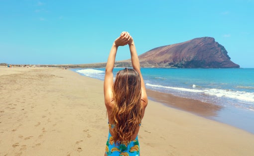 Photo of back view of beautiful woman doing stretching exercises on the beautiful beach in Playa La Tejita, Tenerife.