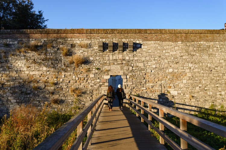 Outdoor of wooden pedestrian bridge cross Jeker canal and small gate entrance of Nieuwenhofstraat Defensive Wall in Autumn season, in Maastricht, Netherlands during evening sunset time.