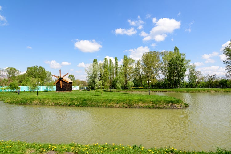 Small lake with a woodmill and an island from Chindiei Park (Parcul Chindiei) in Targoviste, Romania, in a sunny spring day with white clouds and blue sky