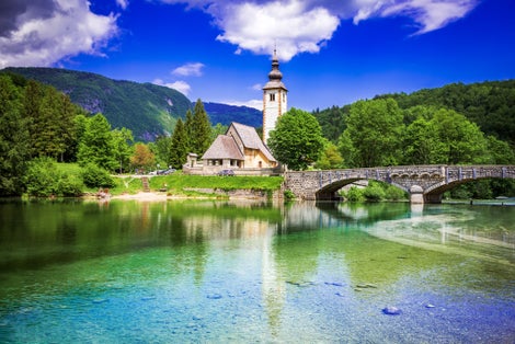 Bohinj Lake, Slovenia. Church of St John the Baptist with bridge over Sava River. Triglav National Park in Julian Alps.