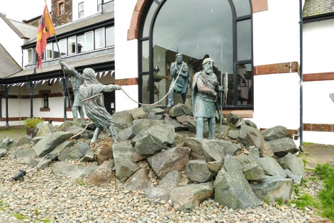 Isle Of Man UK. Peel town. Large sculpture, life size. outside the Manannan Museum depicting four Viking characters among rocks with flag. 