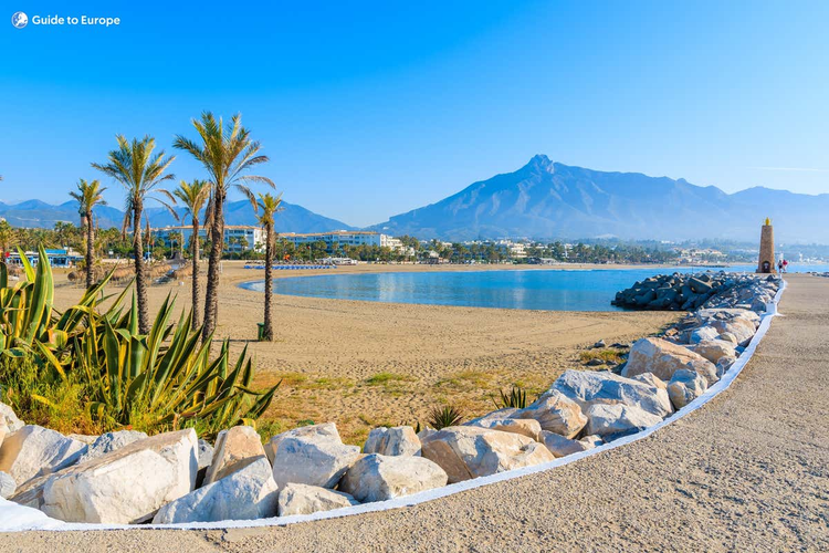 A scenic beach in Marbella, with majestic mountains rising in the background near the Puerto Banus marina..png