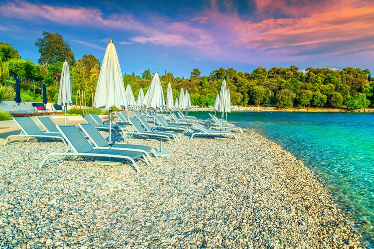 Photo of  gravel beach and seashore. Sun loungers and beach umbrellas at sunset on the beach, Rovinj, Istria region, Croatia.