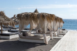 Photo of aerial view of black Perissa beach with beautiful turquoise water, sea waves and straw umbrellas, Greece.