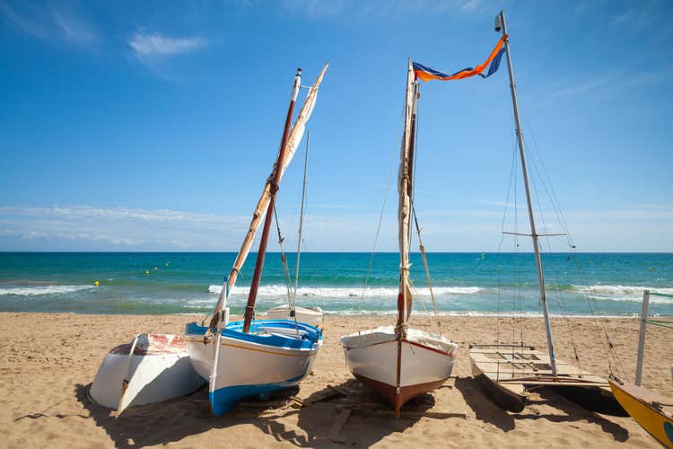 Small sailing boats lay on the sandy beach in Calafell town, coast of Mediterranean sea, Catalonia, Spain.