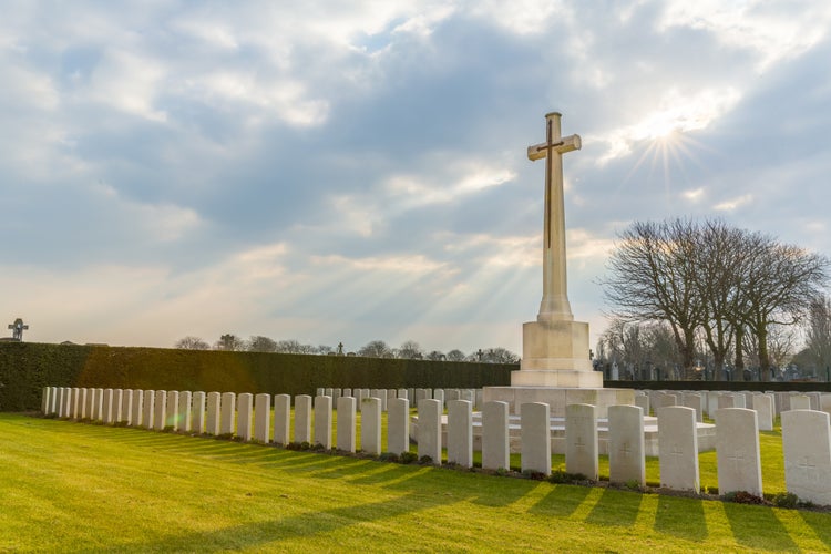 Photo of Cross and Gravestones at the DUNKIRK MEMORIAL CEMETARY, Dunkerque, France with Sun Rays in the cloudy sky.