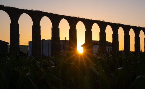 Santa Clara Aqueduct, Vila do Conde, Portugal at sunset with sun shining through arches and vivid orange sky