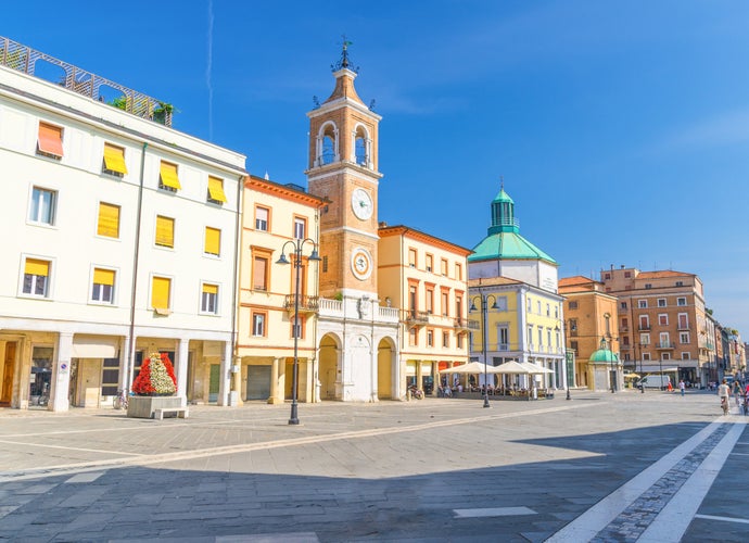 Photo of Piazza Tre Martiri Three Martyrs square with traditional buildings with clock and bell tower in old historical touristic city centre Rimini with blue sky background, Emilia-Romagna, Italy