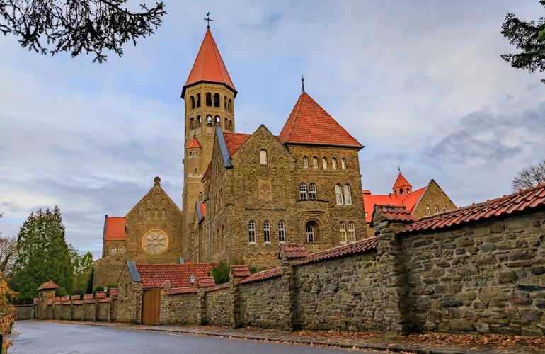 Photo of 19th century neo romanesque Clervaux Abbey, monastery of Saint-Maurice and Saint-Maur Benedictines in Luxembourg surrounded by a forest in the fall.