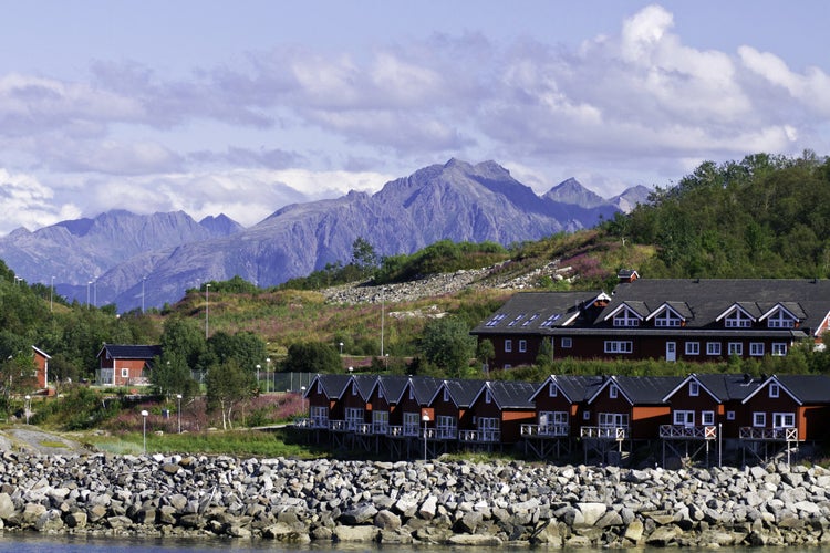 photo of view of Homes along shore protected by stone barrier, with mountains behind in Stokmarknes, Norway