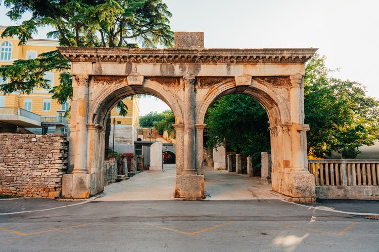 Photo of an aged stone gate surrounded by lush green on a sunny day in Pula, Istria, Croatia.