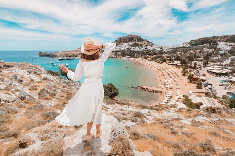 Photo of woman tourist having fun at the stunning view on sea resort and old town of Lindos on the mountain, Rhodes.