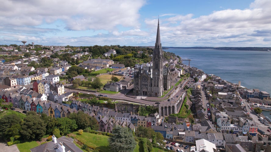 Photo of Aerial view of St. Coleman’s Cathedral and the Deck of Cards, a gravity-defying row of candy-colored houses stacked on a vertiginous hill, in Cobh, Ireland.