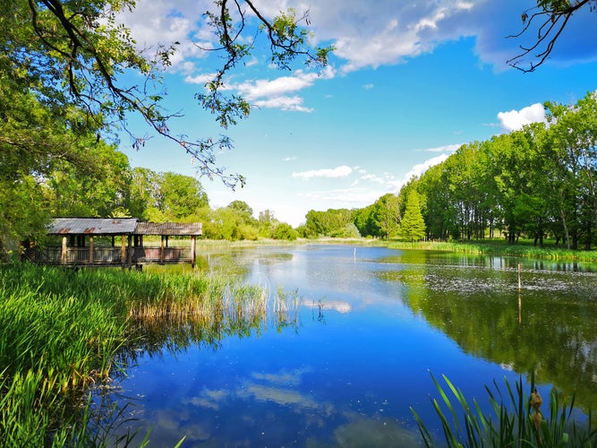 Photo of Small cabin near beautiful lake that reflects the blue sky, beautiful landscape near Craiova, Romania.