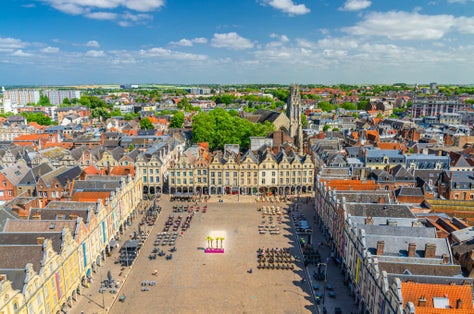 photo of aerial panoramic view of Arras city historical center, Heroes Square with old Flemish-Baroque-style townhouses and John the Baptist catholic church with blue sky in summer day in France.